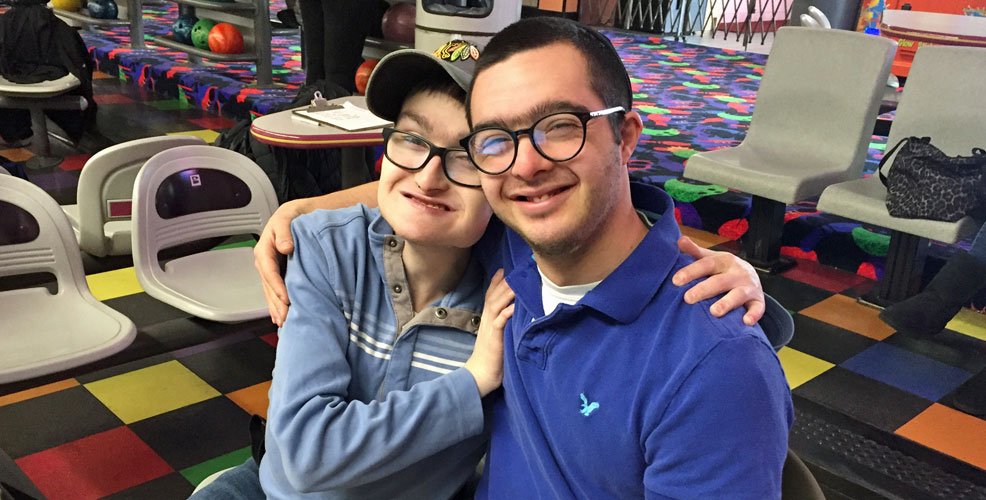 Two friends sitting in a bowling alley with their arms around each other.