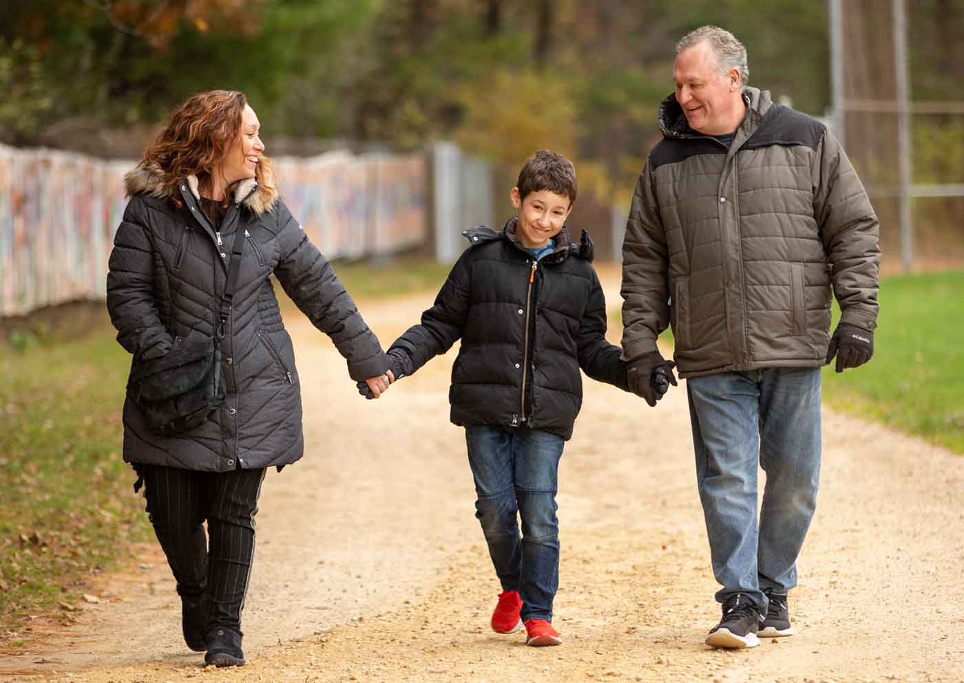 Mom, dad and son holding hands as they walk down a path at Keshet Family Camp.