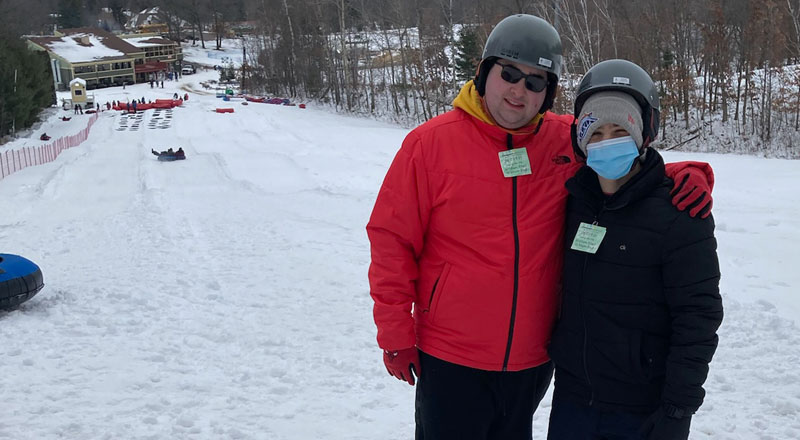 Two teens in full snow gear standing on top of the snow tubing hill