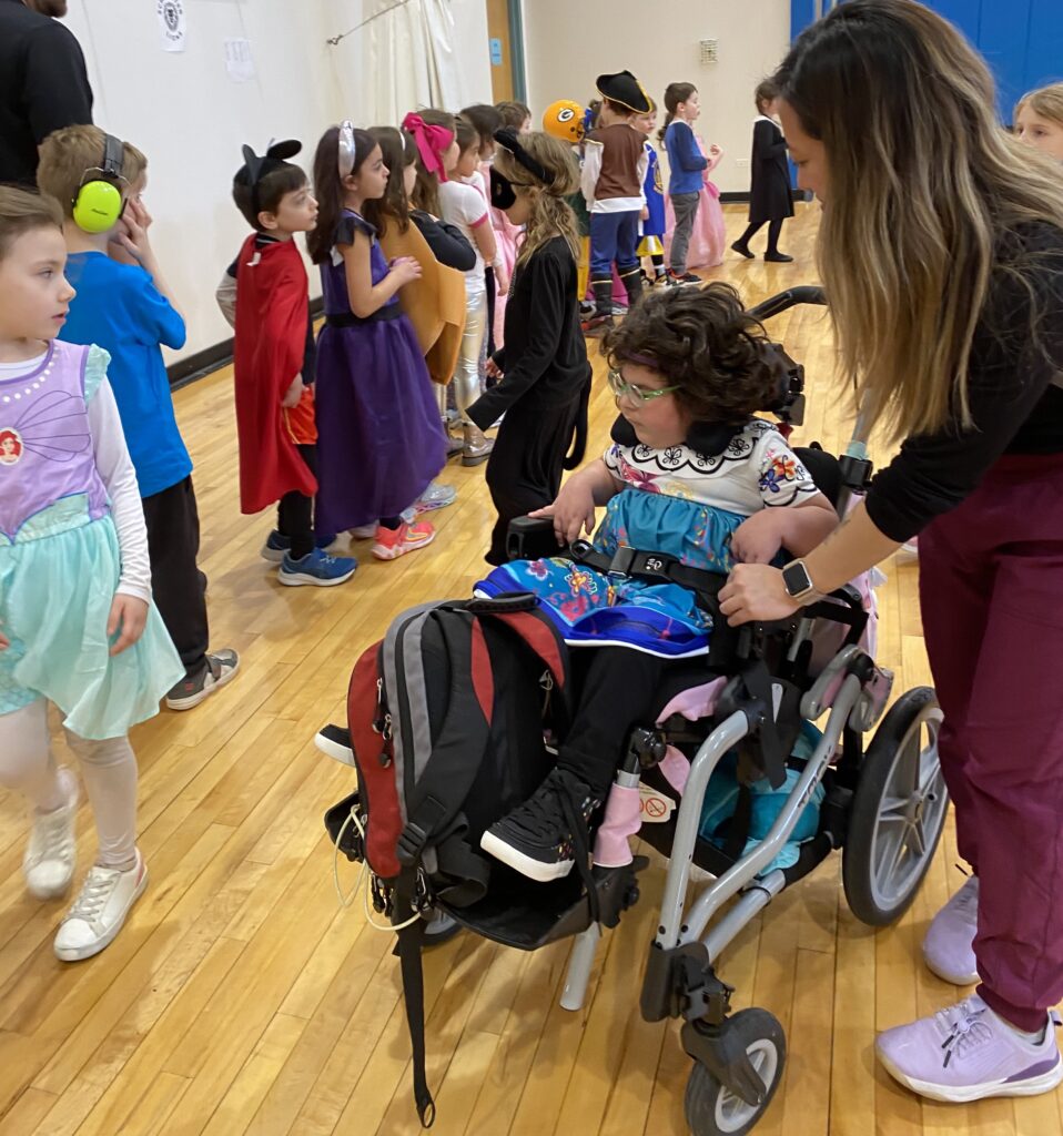 Keshet Day School student in a wheelchair lined up next to a bunch of Schecther students in Purim costumes