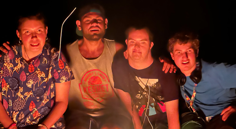 Four staff with their arms around each other sitting in front of a camp fire
