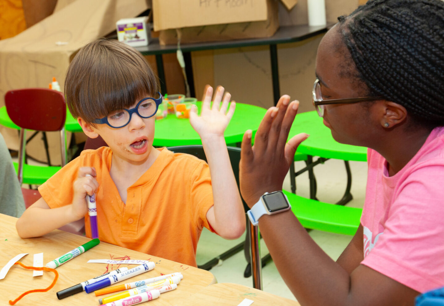 Counselor and camper high fiving each other with markers in front of them