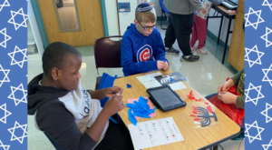 Schechter and Keshet student working on the stained glass craft with a Blue and white menorah background