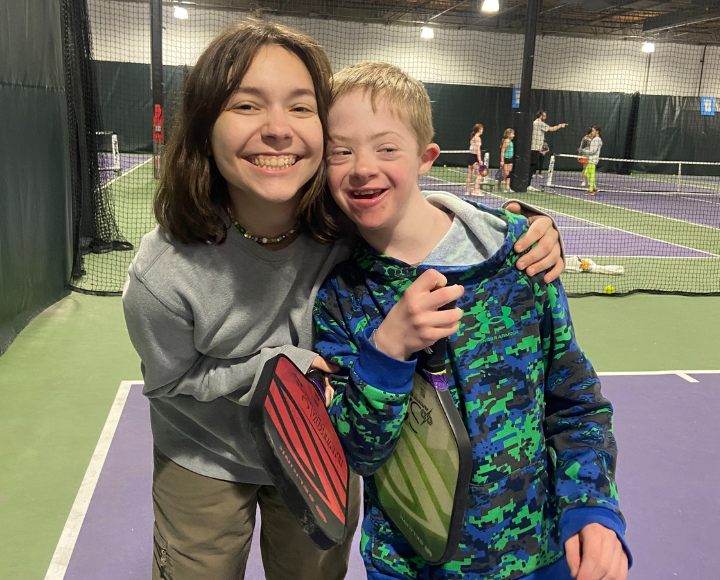 Volunteer and participant hugging and holding pickleball paddles