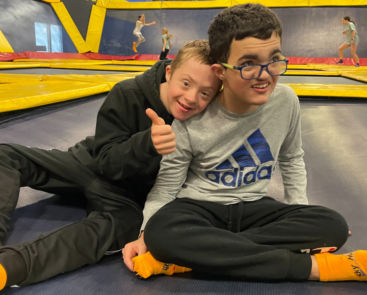 Two friends sitting on a trampoline with their thumbs up