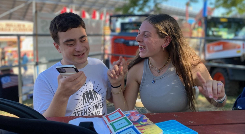 Harrison laughing with a camper outdoors and playing on his phone and with his schedule