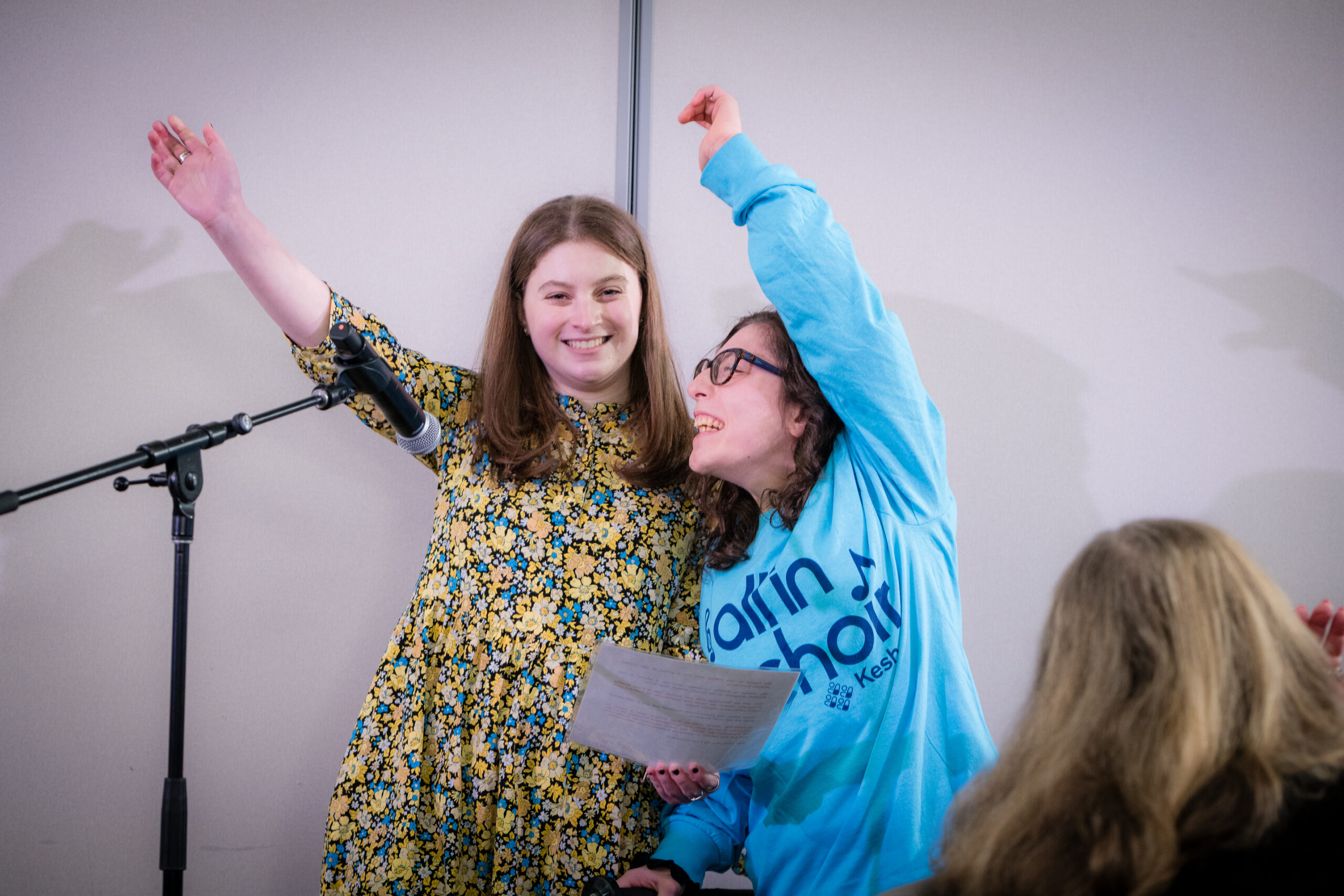 Keshet student and Ida Crown student with their arms in the air while they deliver a speech at the banquet