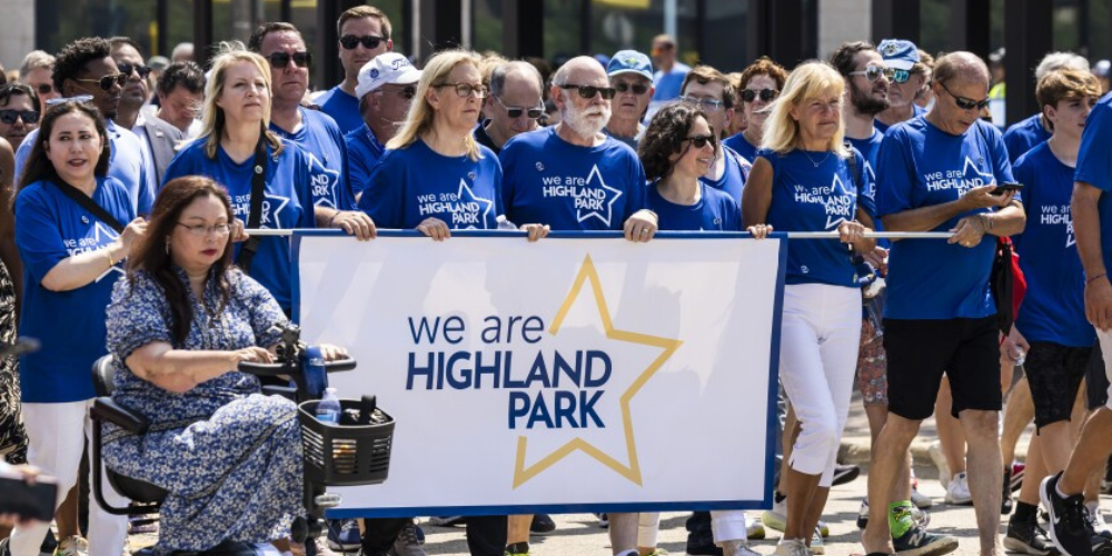 Highland Park community members walking together wearing shirts and holding a sign that says "We are Highland Park"
