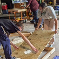 Two people moving wood to construct corn hole