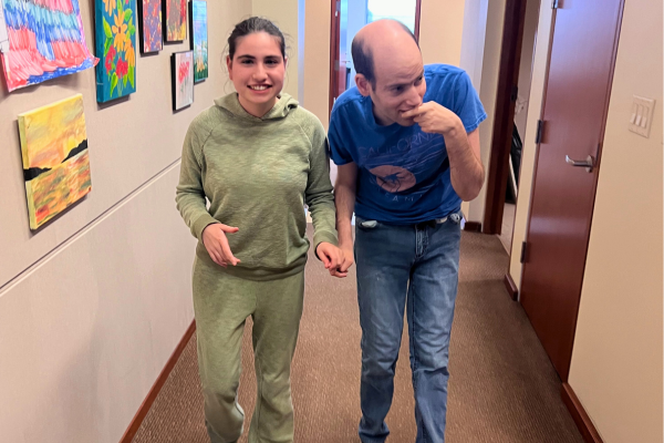 Two adult participants walking down a hallway and holding hands