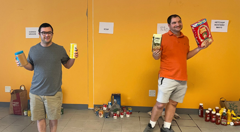 Two team members standing in the PORCH warehouse holding up donated food items