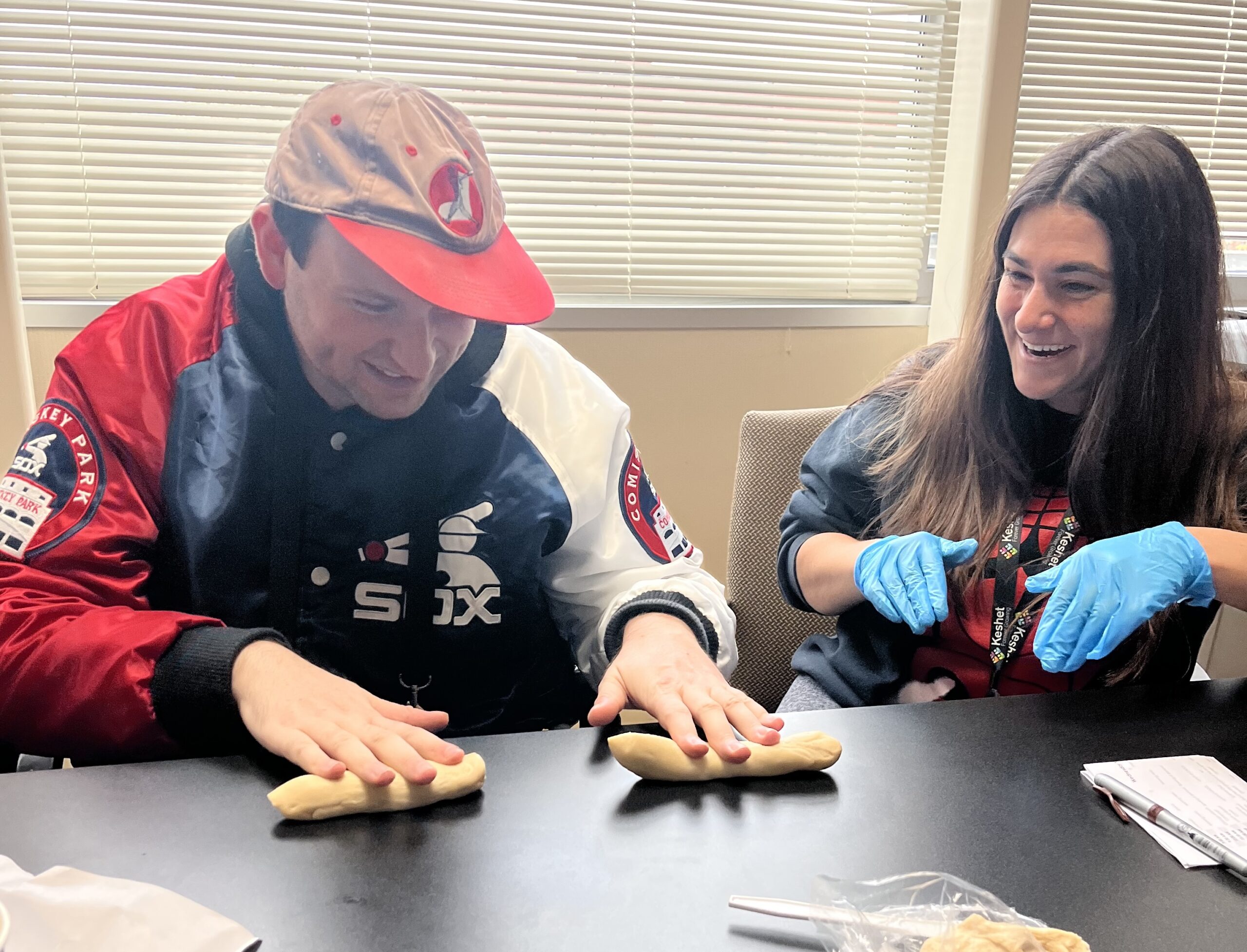 Participant and staff smiling while they roll challah dough