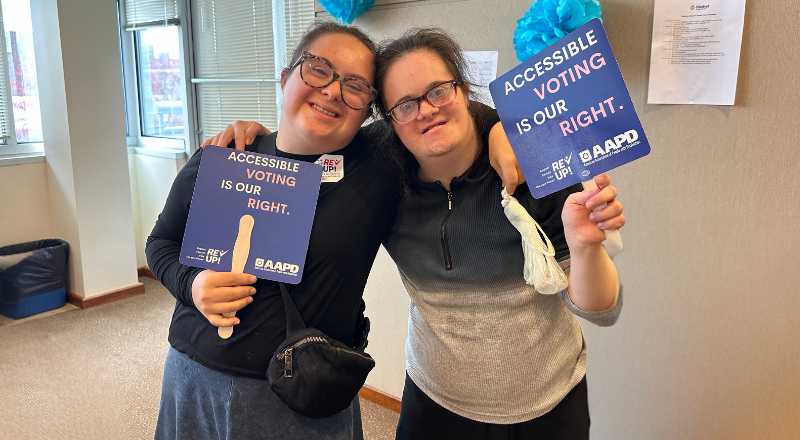 Two adult women standing together and holding signs that say "accessible voting is our right"