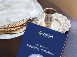 Table with a seder plate and a copy of the Keshet haggadah on the table
