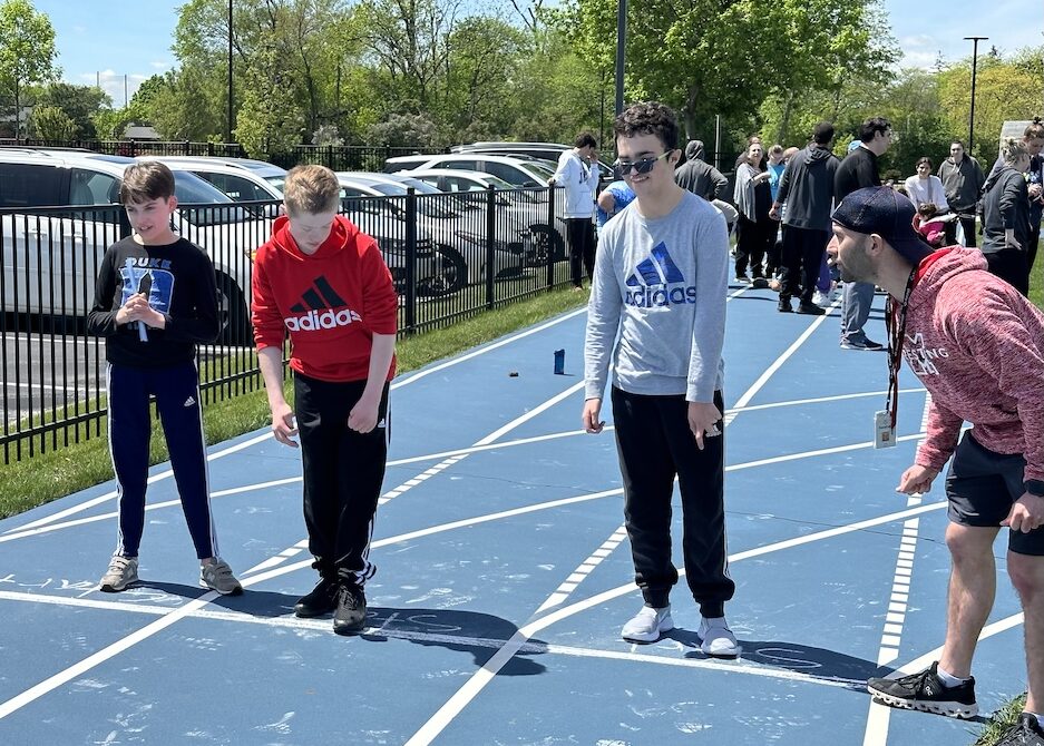 Three athletes at the track starting line with the coach standing on the side