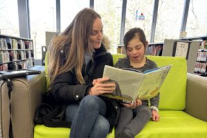 student and staff reading a book together at the library