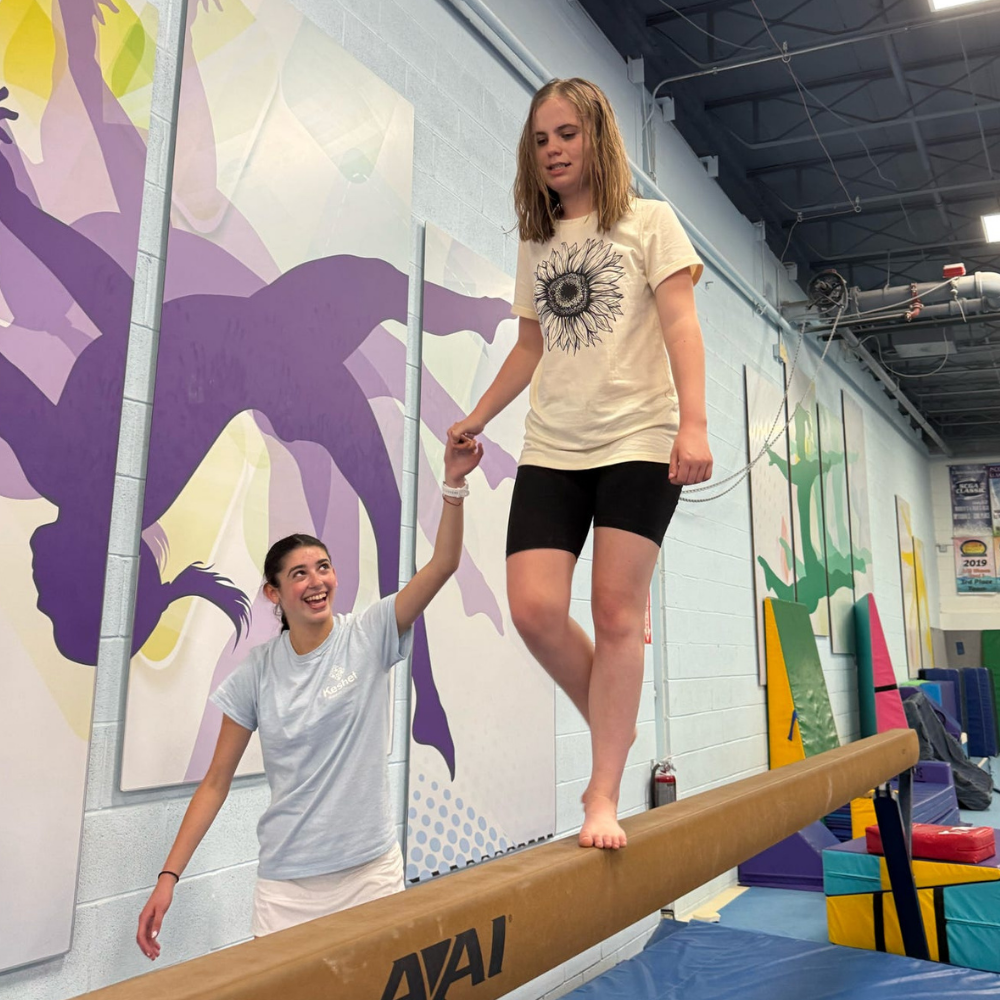 Camper walking on a balance beam while counselor holds their hand