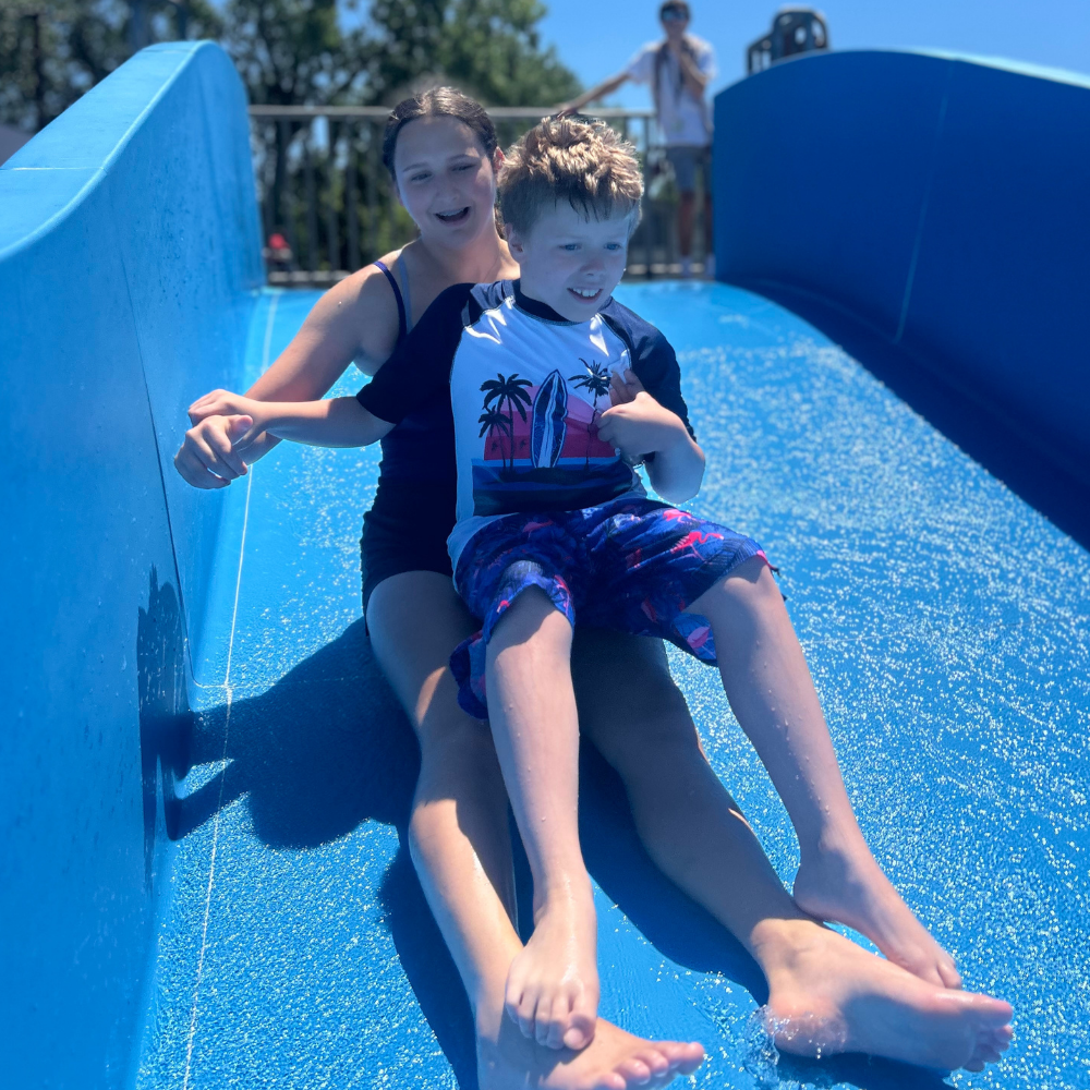 counselor sliding on a slide while a camper sitting on their lap