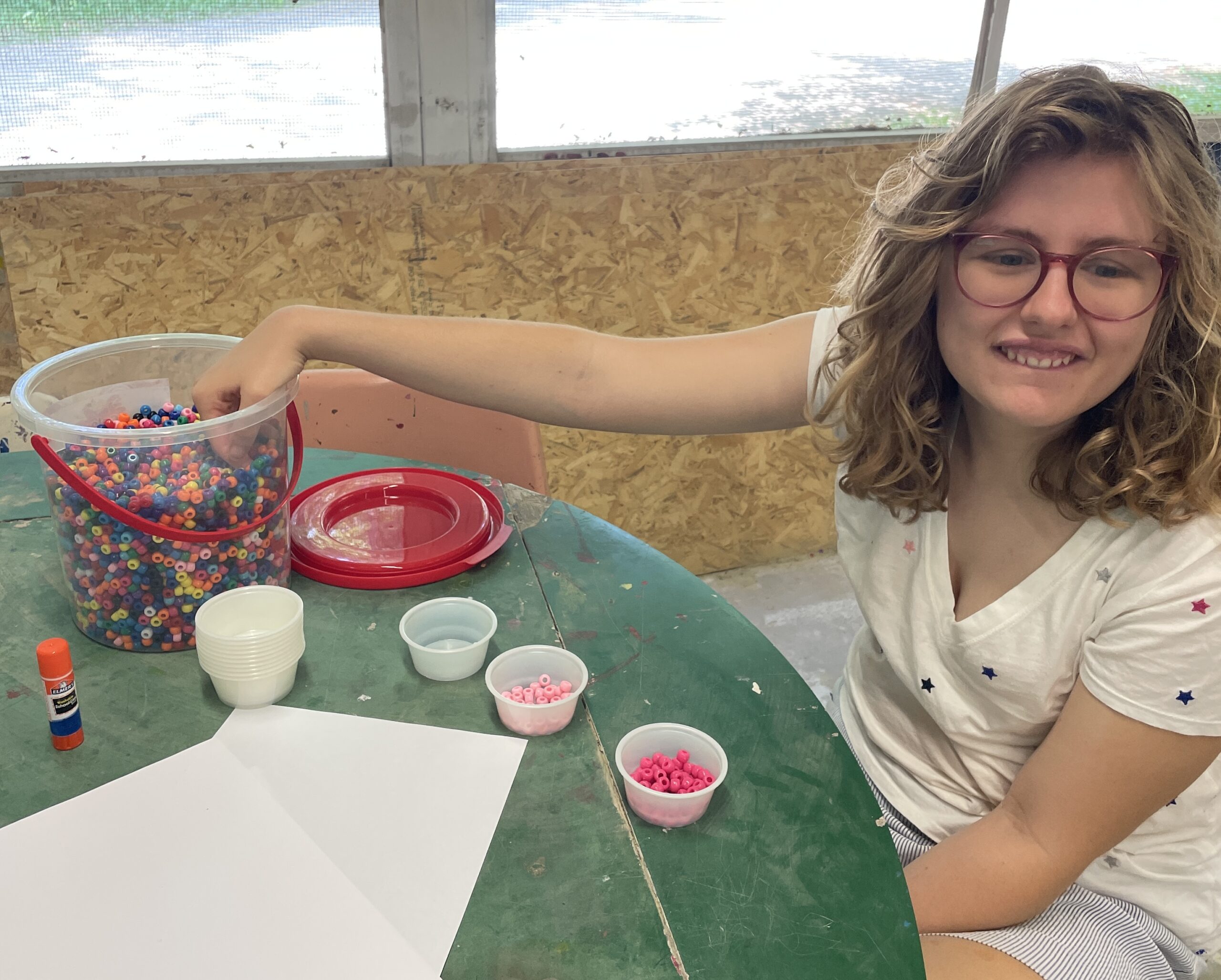 Cathy smiling while placing her hand in a container of beads at the art center