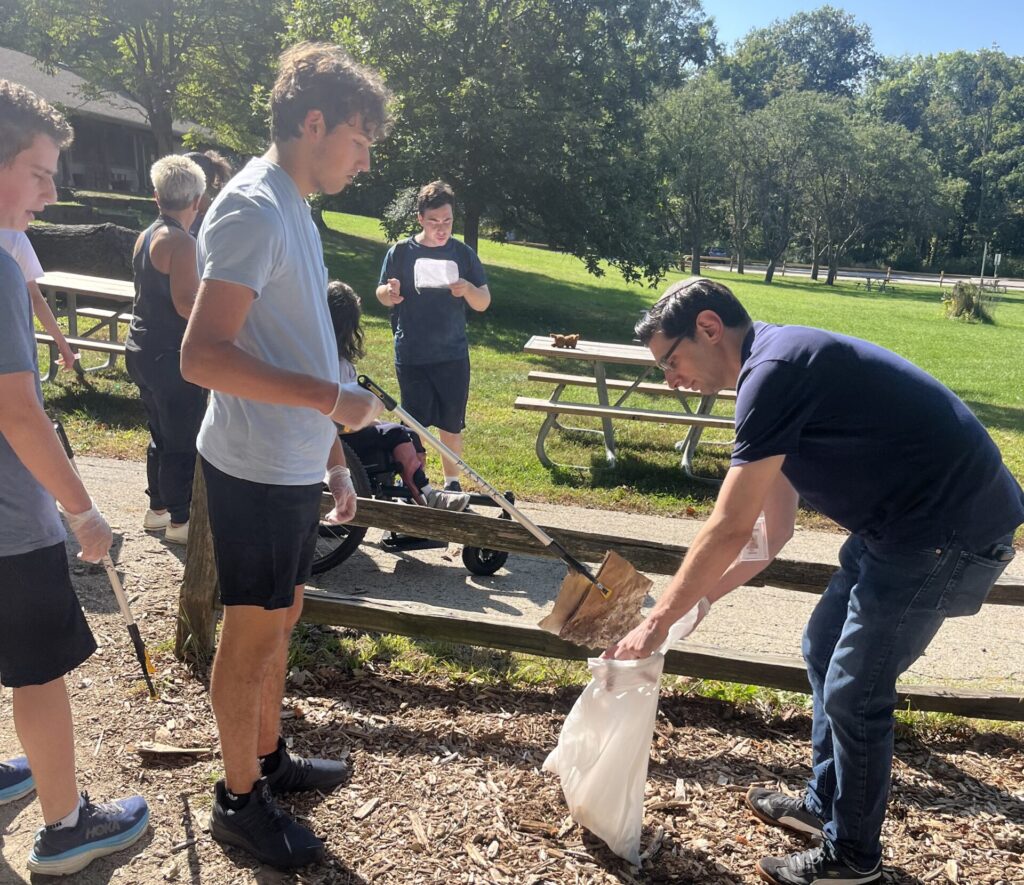 Teen scooping garbage into a bag that a staff is holding