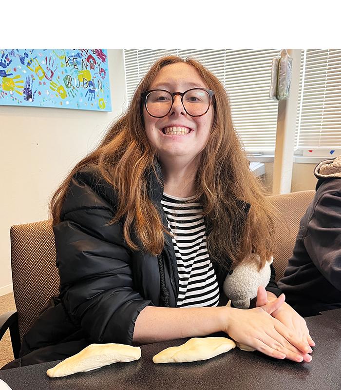 Adult smiling while sitting a table and rolling challah dough
