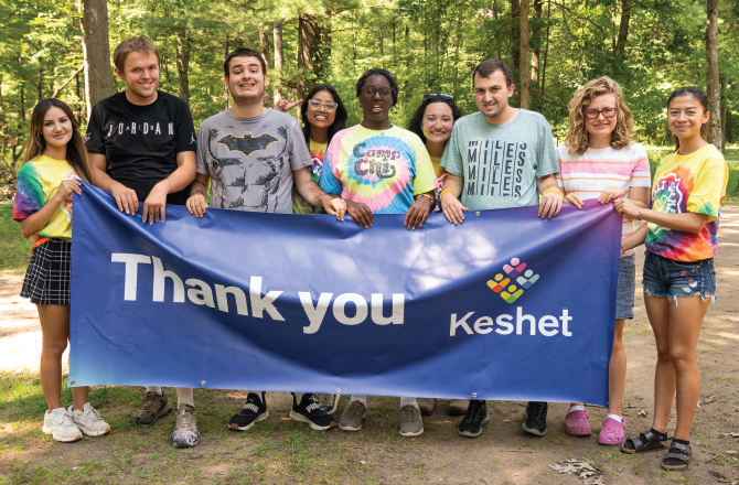 Group of campers and counselors standing and holding a large banner that says