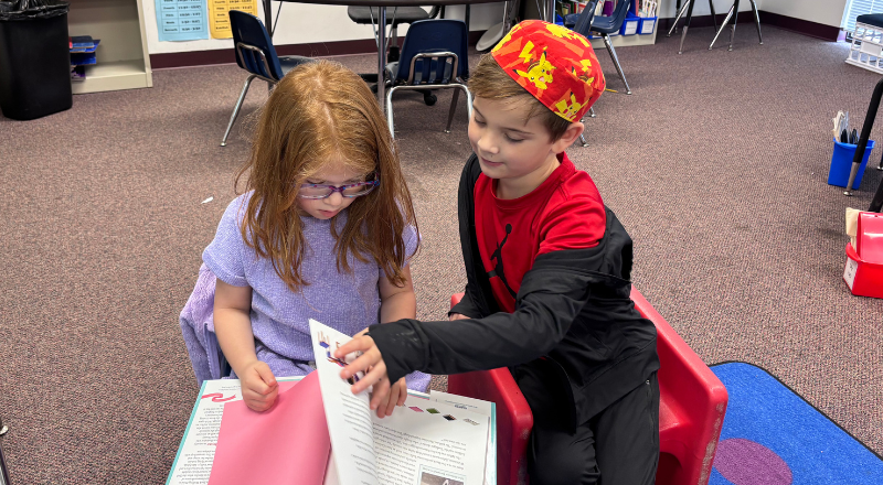 Two students sitting and reading a book together
