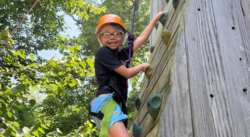 Camper climbing a rock wall and smiling