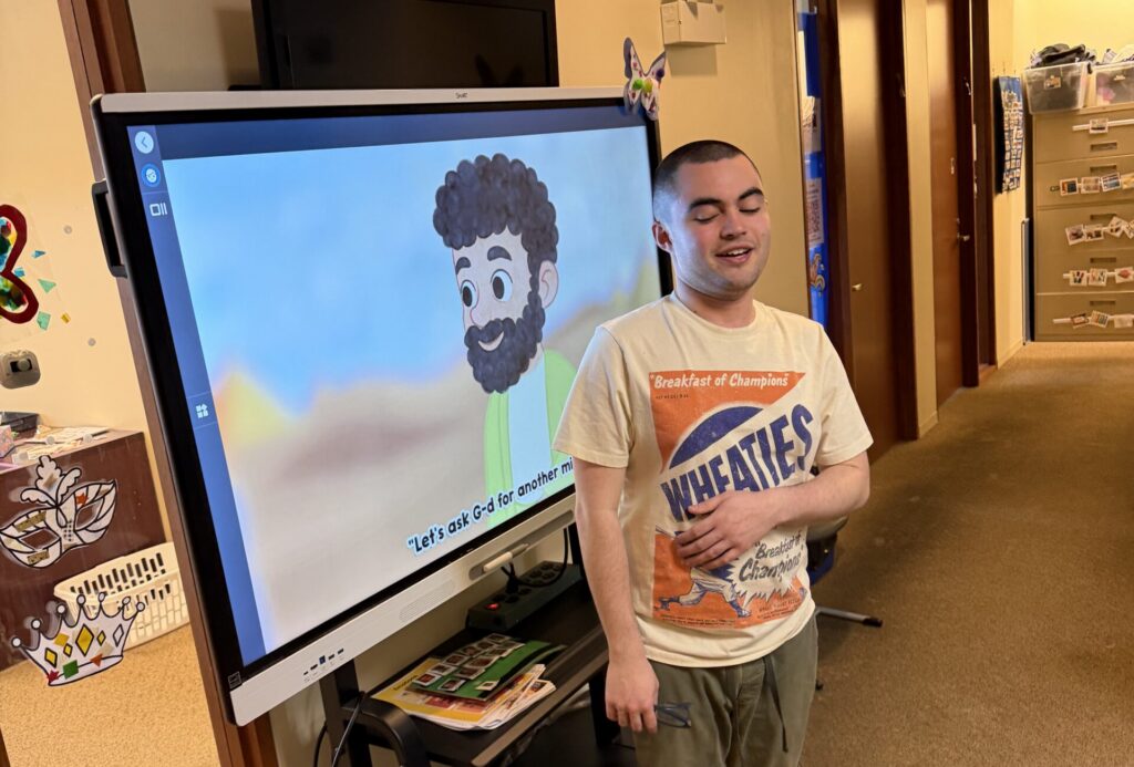 Student standing in front of screen showing an animation of the passover story