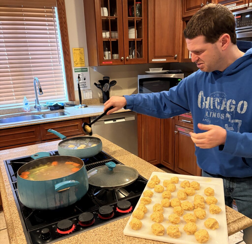 Adult in a kitchen mixing matzo balls into soup broth