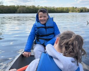 Camper smiling while sitting in a rowboat and looking at his counselor