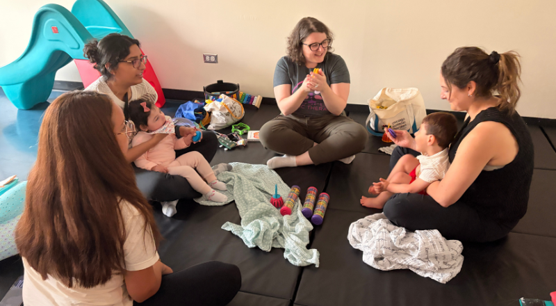 group of parents and babies sitting on a mat with instructors