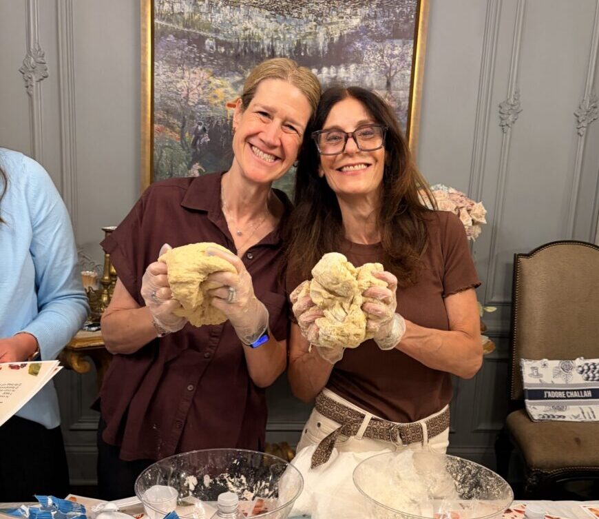 Two moms holding challah dough and smiling